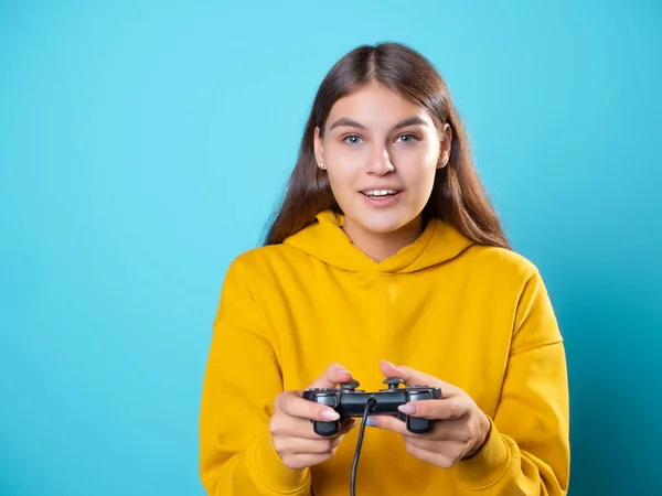 Een gamer meisje, een jonge brunette in een gele hoodie, grijpt een gamepad in haar handen — Stockfoto