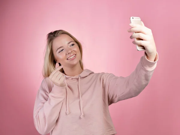 Jovem atraente em um capuz rosa usa um smartphone para comunicação de vídeo. — Fotografia de Stock