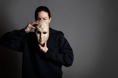 Saklan, kasvetli genç bir kadın yüzünü maskenin arkasına gizliyor.