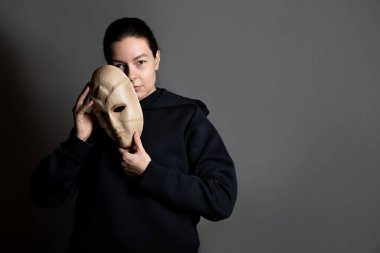 Maskenin arkasına saklanan koyu renk kapüşonlu genç bir kadın yüzünü maskeyle gizliyor.,