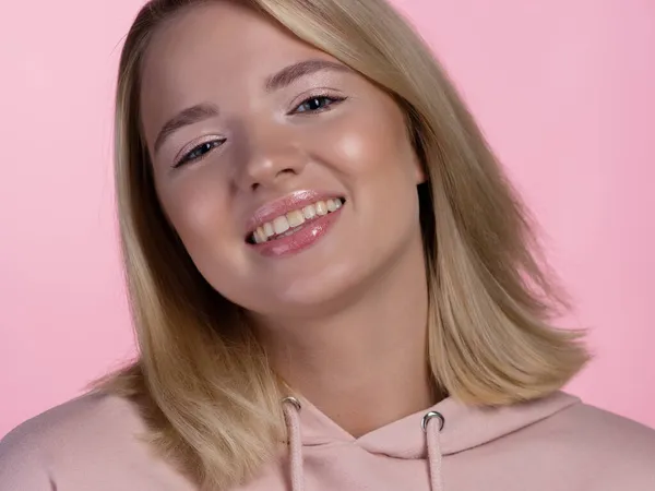 Süße junge Blondine im rosa Kapuzenpulli lächelt glücklich. — Stockfoto