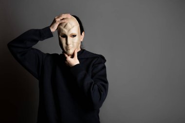 İsimsiz bir yabancı, siyah kapüşonlu bir kadın yüzünü maskeyle örtüyor.,