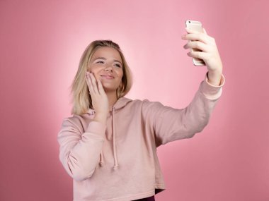 Pembe kapüşonlu çekici genç kadın video ya da fotoğraf çekmek için akıllı telefon kullanıyor..