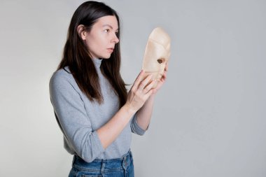 Genç bir kadın yüzünü bir maskenin arkasına gizler. Psikolojik sorunlar kavramı.,