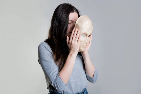 O femeie tânără își ascunde fața în spatele unei măști, conceptul de cosmetologie — Fotografie, imagine de stoc