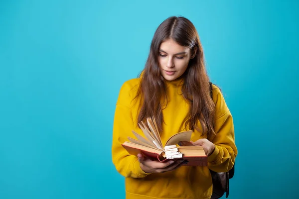 En ung student med ryggsäck tittar på en bok och läser. — Stockfoto