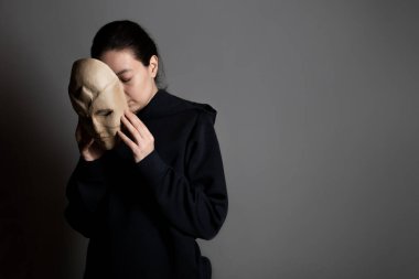 Maskenin arkasına saklanan koyu renk kapüşonlu genç bir kadın yüzünü maskeyle gizliyor.,