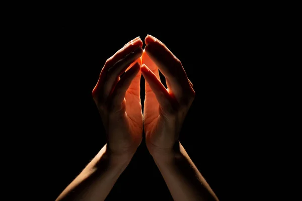 Belas mãos dobradas com luz no topo, fundo preto. Oração ou criação de um milagre. — Fotografia de Stock