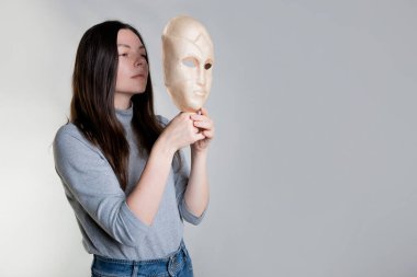 Genç bir kadın yüzünü bir maskenin arkasına gizler, kozmetoloji kavramı.