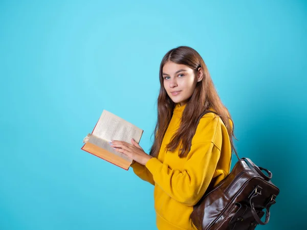 Un joven estudiante con una mochila mira un libro y lee. — Foto de Stock