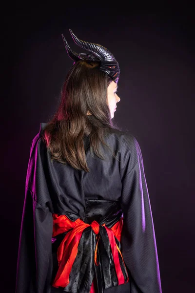 Une démone avec des cornes et dans un kimono noir avec une ceinture rouge, — Photo