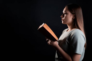 Kitap okumak, bir roman okumak ya da zevk almak. Açık bir kitabı olan, tişörtlü esmer bir kız.