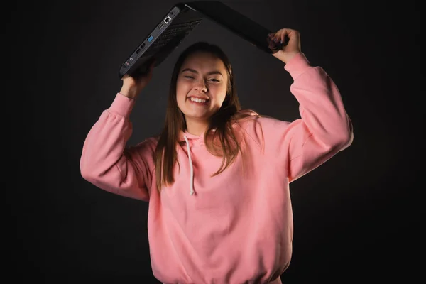 A happy student or freelancer with a laptop in her hands. A young charming woman in a pink hoodie — Stockfoto