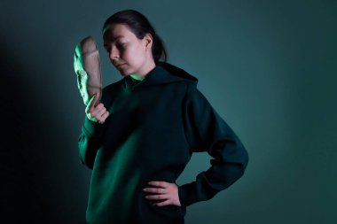 Maskenin arkasına saklanan koyu renk kapüşonlu genç bir kadın yüzünü maskeyle gizliyor.,