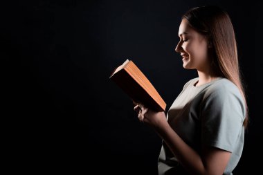 Kitap okumak, bir roman okumak ya da zevk almak. Açık bir kitabı olan, tişörtlü esmer bir kız.