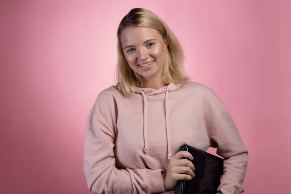 Mladá žena s laptopem, studentkou nebo na volné noze. Okouzlující blondýna v růžové mikině — Stock fotografie