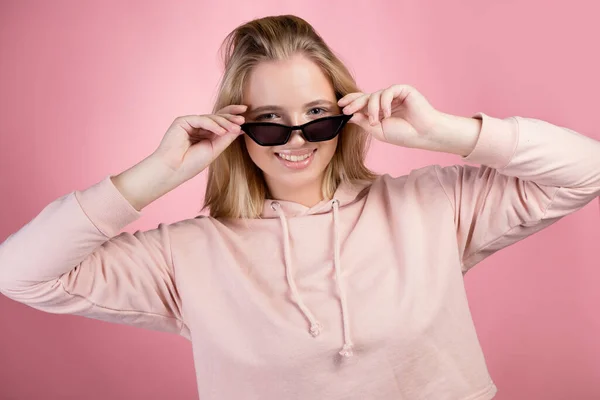 Stylová mladá a módní blondýna v růžové přerostlé mikině a černých slunečních brýlích, — Stock fotografie