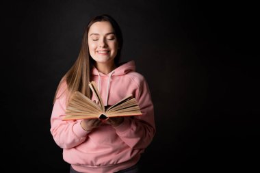 Pembe kapüşonlu bir esmer, kitap okuyor. Elinde açık bir kitapla bir öğrenci.,