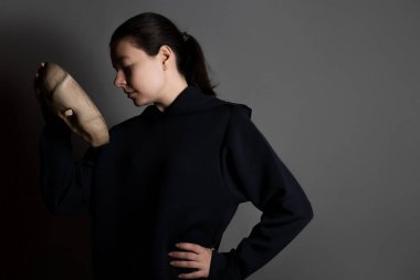 Maskenin arkasına saklanan koyu renk kapüşonlu genç bir kadın yüzünü maskeyle gizliyor.,