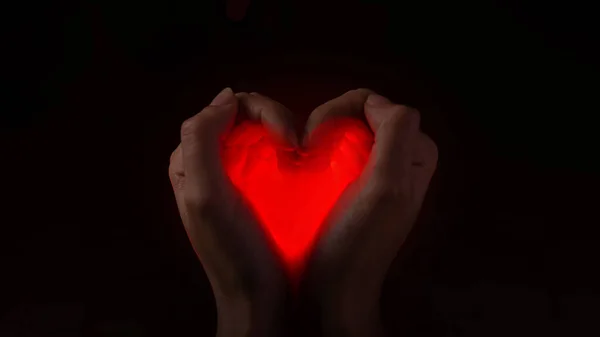 Un corazón resplandeciente en las manos doblado en forma de corazón, un concepto artístico de amor y cuidado. — Foto de Stock