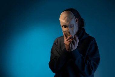 Maskenin arkasına saklanan koyu renk kapüşonlu genç bir kadın yüzünü maskeyle gizliyor.,