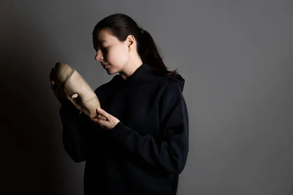 Hiding behind a mask, a young woman in a dark hoodie hides her face with a mask, Stock Photo