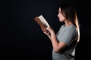 Kitap okumak, bir roman okumak ya da zevk almak. Açık bir kitabı olan, tişörtlü esmer bir kız.