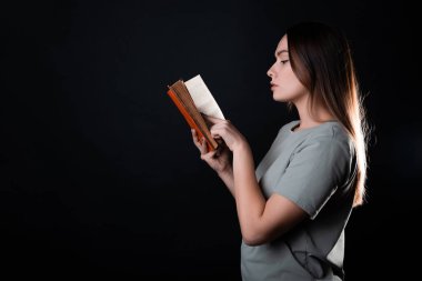 Kitap okumak, bir roman okumak ya da zevk almak. Açık bir kitabı olan, tişörtlü esmer bir kız.