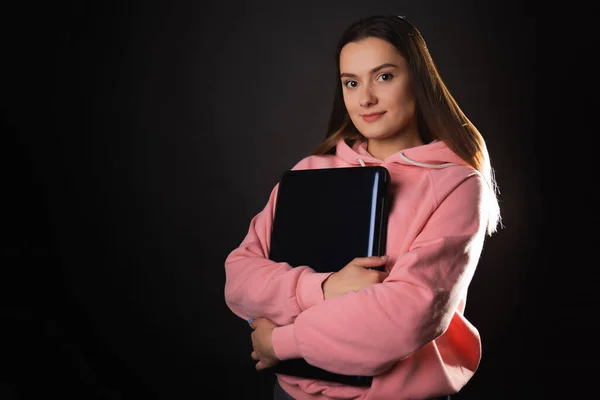 A student or a freelancer with a laptop in her hands. A young charming woman in a pink hoodie works remotely. — Stock fotografie