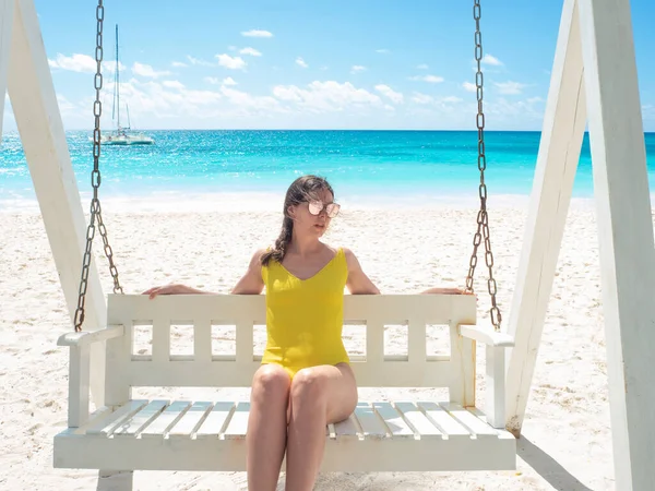 Un viajero feliz en traje de baño amarillo en una playa con arena blanca y agua azul clara. — Foto de Stock