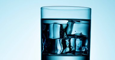 Mavi zemin üzerinde bir bardak su nükteli buz.