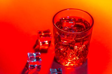 Arkaplanda buz küpleri olan bir bardak su.