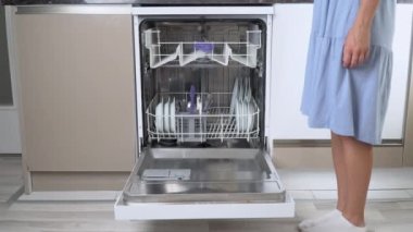 Bir ev hanımı bulaşık makinesinin boş üst rafını alt rafı dolu bir şekilde dışarı itiyor. Yüksek kalite 4k görüntü
