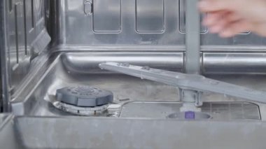 Bir kadın bulaşık makinesinin eline bulaşık deterjanı döküyor.