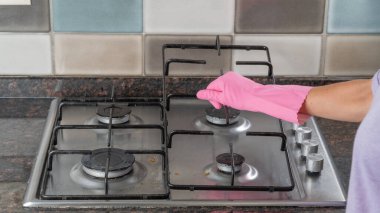 Bir kadın lastik eldiveni tutarak yüzeyi yıkamak için gaz sobasının ızgarasını tutar.