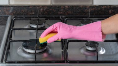 Pembe lastik eldivenli bir kadın eli gaz sobasını süngerle yıkıyor.