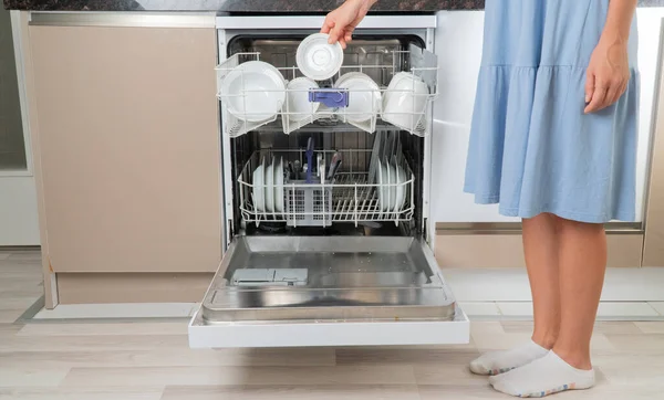 家庭主妇从洗碗机前把干净的碗碟拿走 — 图库照片