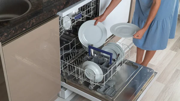 Housewife pulls clean plates out of dishwasher close-up