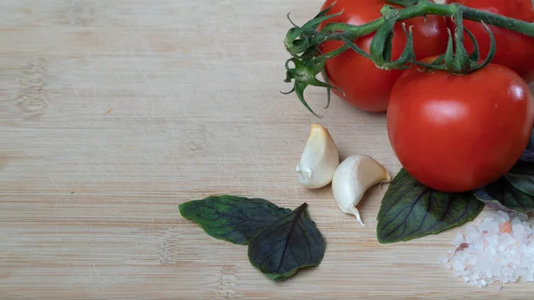 Tomatoes on a branch, garlic, basil and coarse sea salt on a wooden background with space for inscription. High quality photo