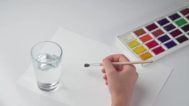 Bir kadın eli çizim fırçası ve suluboya ile fırçayı bir bardak temiz suda nemlendirir. Yüksek kalite 4k görüntü