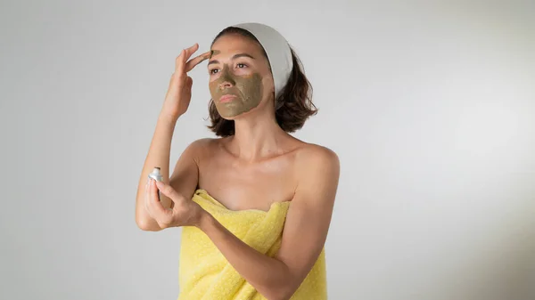 Woman in a towel makes a face mask - home care for the skin of the face. High quality photo