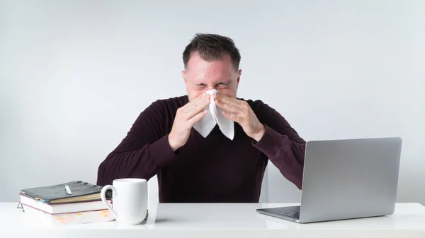 A man with a runny nose in the workplace in the office - get the flu at work. High quality photo