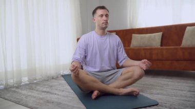 Bir adam evde lotus pozisyonunda meditasyon yapar, bilinçli nefes alma pratiği. Yüksek kalite 4k görüntü
