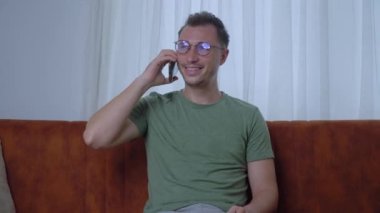 Gözlüklü bir adam evin kanepesinde otururken telefonla iletişim kuruyor. Yüksek kalite 4k görüntü