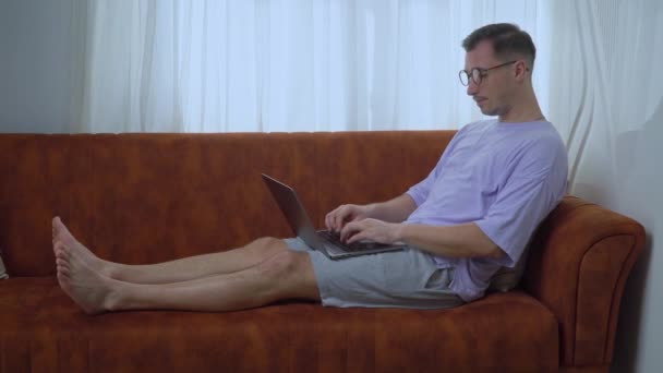 パソコンに眼鏡をかけた男がソファの上で働いていた 高品質4K映像 — ストック動画