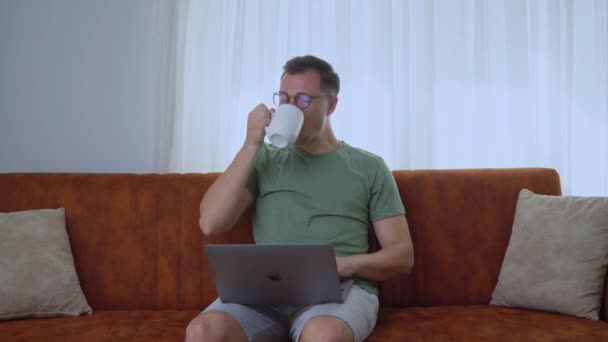 Egy Férfi Egy Laptopnál Dolgozik Otthon Kanapén Kávét Iszik Kiváló — Stock videók