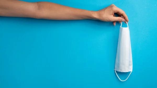 Bir kadının eli mavi arka planda bir maske tutar, mesaj için bir yer. Yüksek kalite fotoğraf