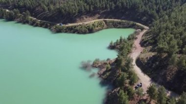 Ormandaki göl boyunca yılan gibi kıvrılan toprak yol, hava fotoğrafçılığı.