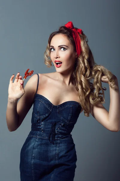 Portret sexy blonde vrouw in jeans sundress en rode pin-schoenen up retro vrouw meisje met een lolly rode cockerel zuigt een lolly rode cockerel — Stockfoto