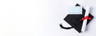 Mezuniyet karesi akademik şapkasının üst görünümü diploma ve maske beyaz masa arkasında izole.